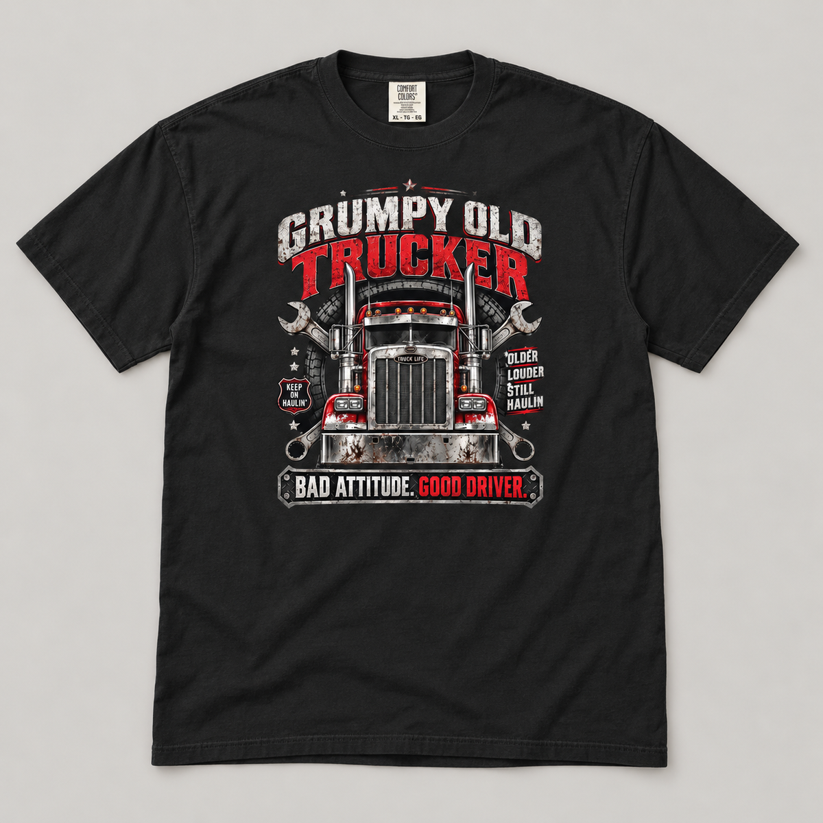 AI flat-lay mockup of a Black Grumpy Old Trucker T-shirt on a light grey surface, showing the red semi-truck, crossed wrenches and Bad Attitude. Good Driver. front graphic.