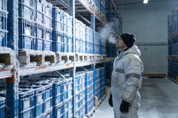 A cold storage warehouse worker in an insulated freezer suit and beanie standing near frosted freezer racks