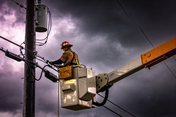A lineman in a bucket truck working on a utility pole against a stormy sky