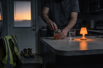 A night shift worker opens a jar of magnesium gummies on his kitchen counter at sunrise, his hi-vis vest and work boots by the door behind him.