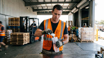 Warehouse worker mixing electrolyte powder into a shaker bottle at a hot loading dock