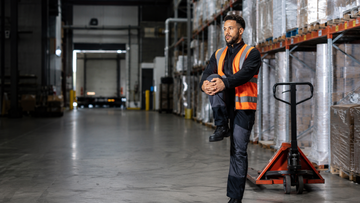 Warehouse worker stretching knee and wrist after a physically demanding shift