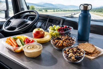 Healthy portable snacks arranged inside a truck cabin, including fruit, vegetables, nuts, hummus, crackers, and water.