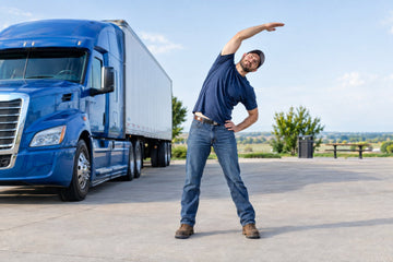 A truck driver stretches beside a parked semi-truck at a rest area.