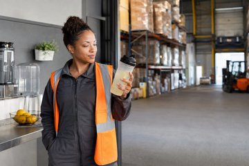 Warehouse worker holding a clear citrus-colored protein beverage during a shift break