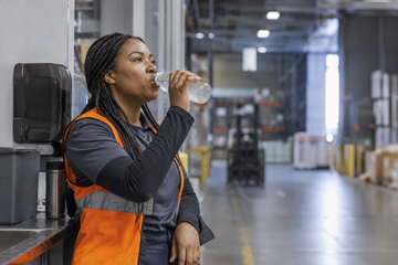 Warehouse worker drinking water during a break as part of a long-shift hydration routine