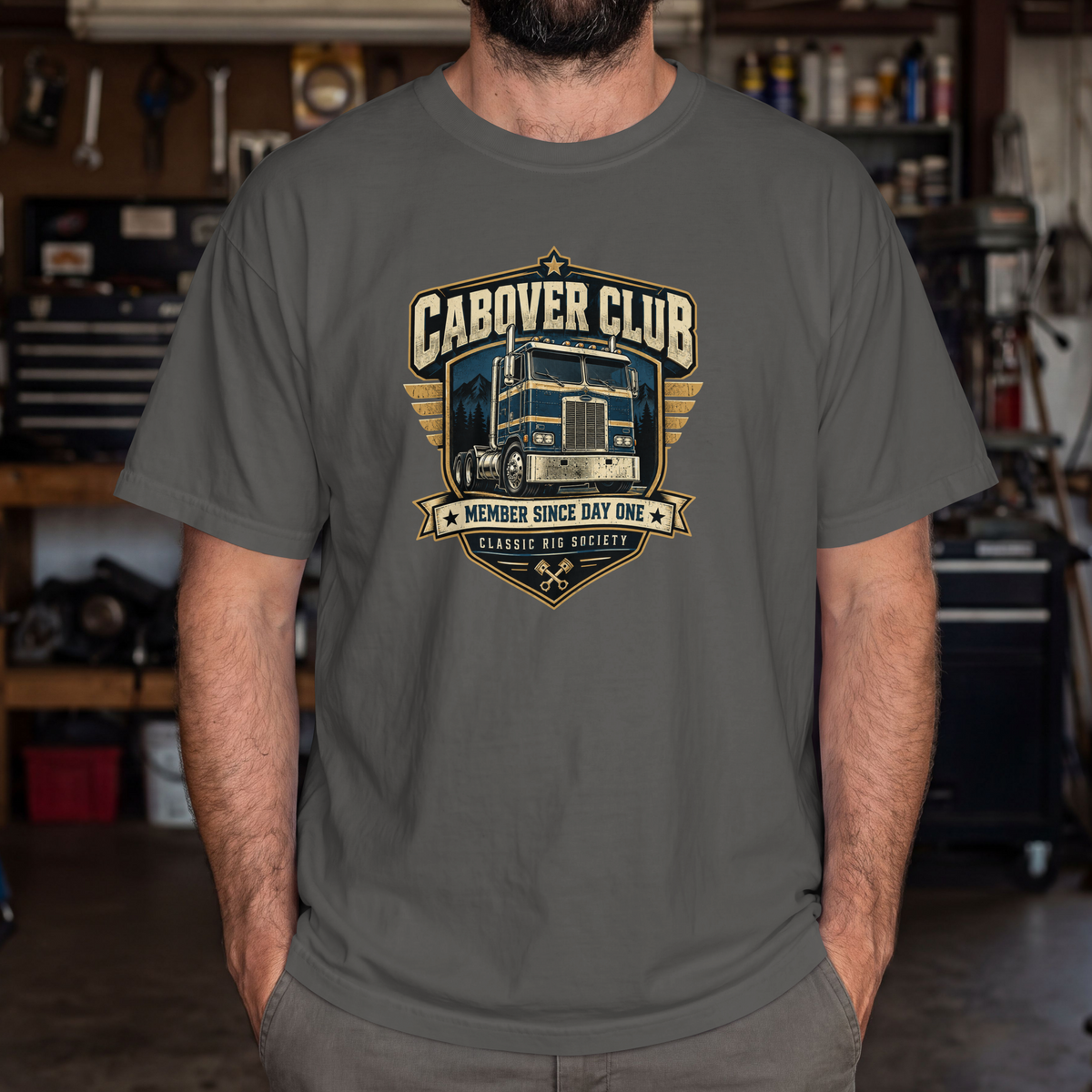 Pepper Cabover Club T-shirt with blue and gold vintage cabover truck graphic and Member Since Day One lettering, male model in workshop.