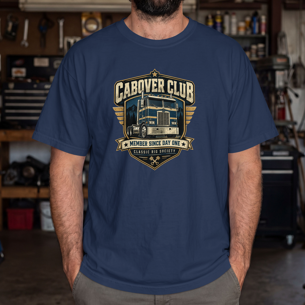 True Navy Cabover Club T-shirt with blue and gold vintage cabover truck graphic and Member Since Day One lettering, male model in workshop.