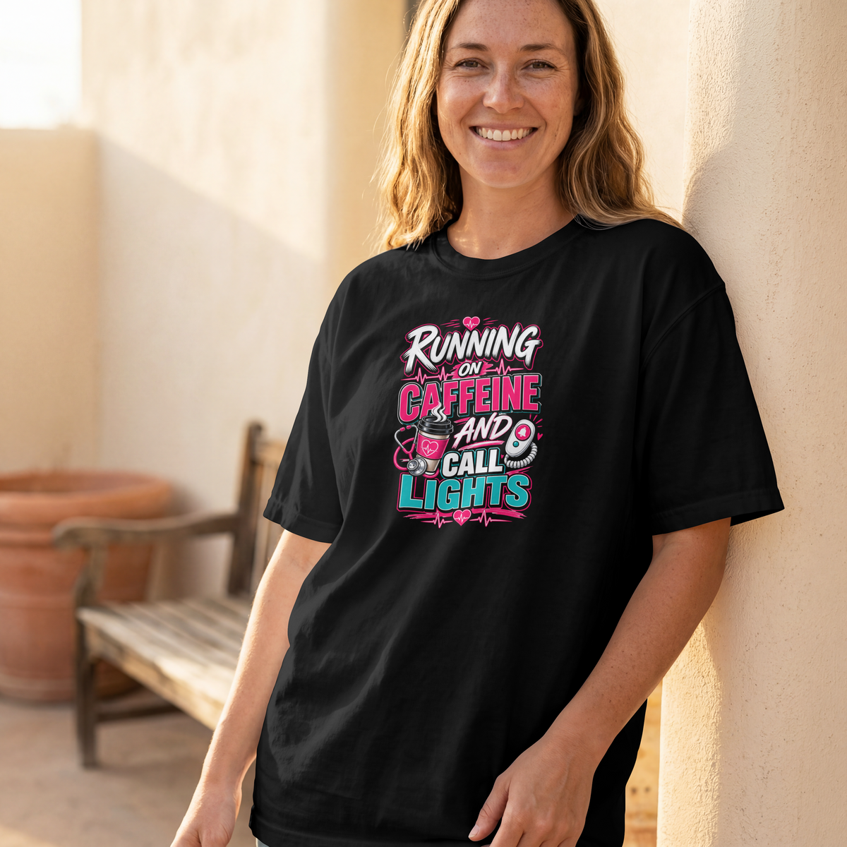 Nurse wearing the black Running on Caffeine and Call Lights tee, leaning against a stucco wall outdoors