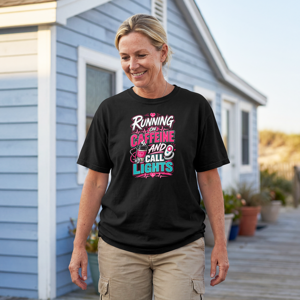 Nurse wearing the black Running on Caffeine and Call Lights tee outside a house on a boardwalk