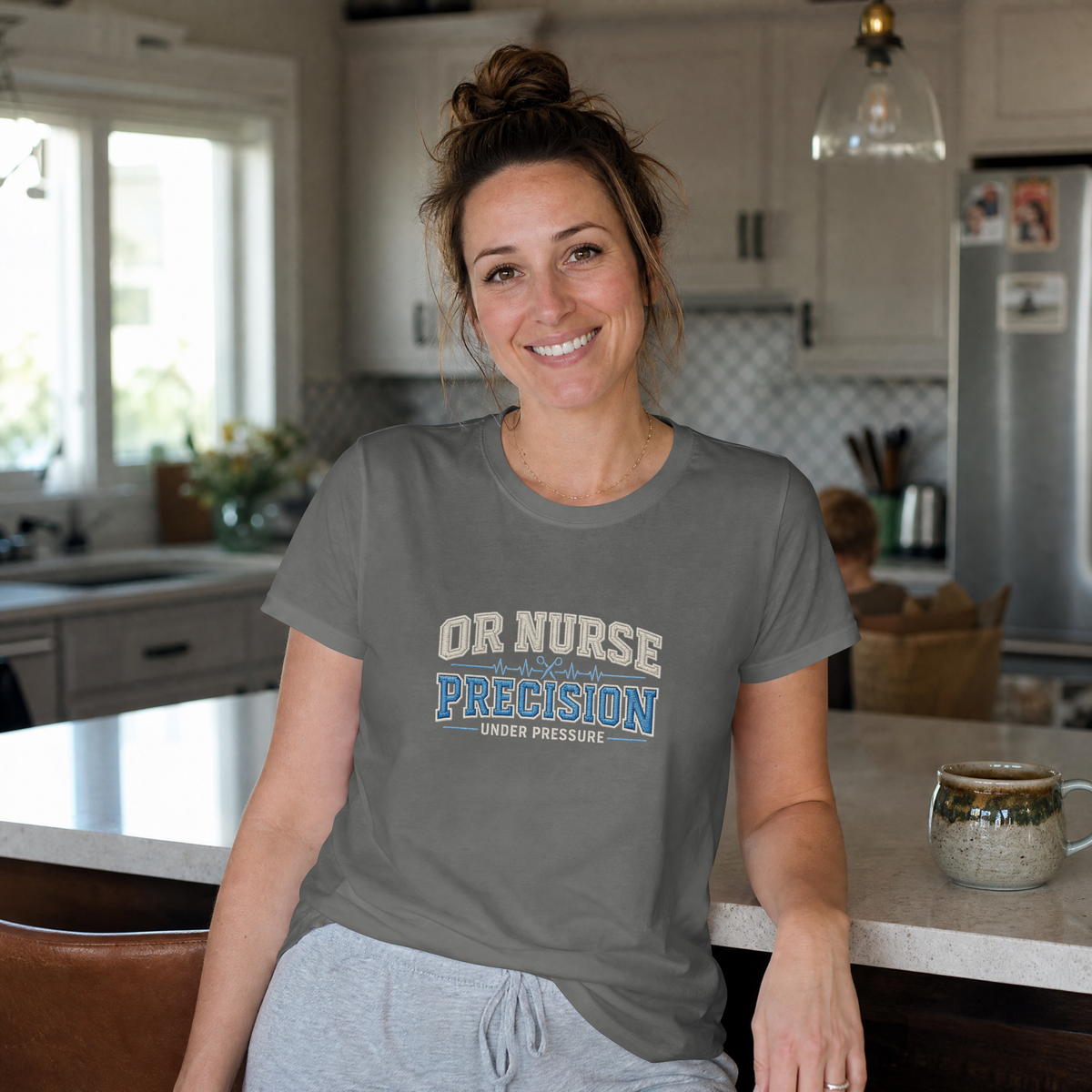 Woman wearing a Pepper gray OR Nurse Precision Under Pressure T-shirt while leaning on a kitchen counter.