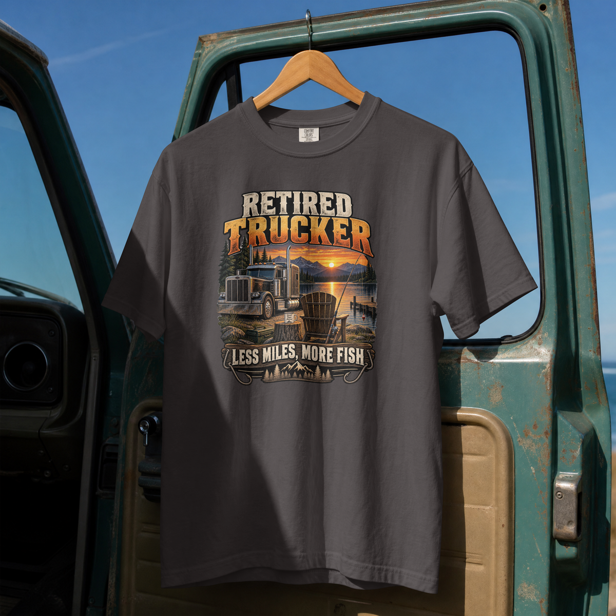 Graphite Retired Trucker Less Miles More Fish T-shirt, full front hanging view with truck and lakeside fishing graphic.