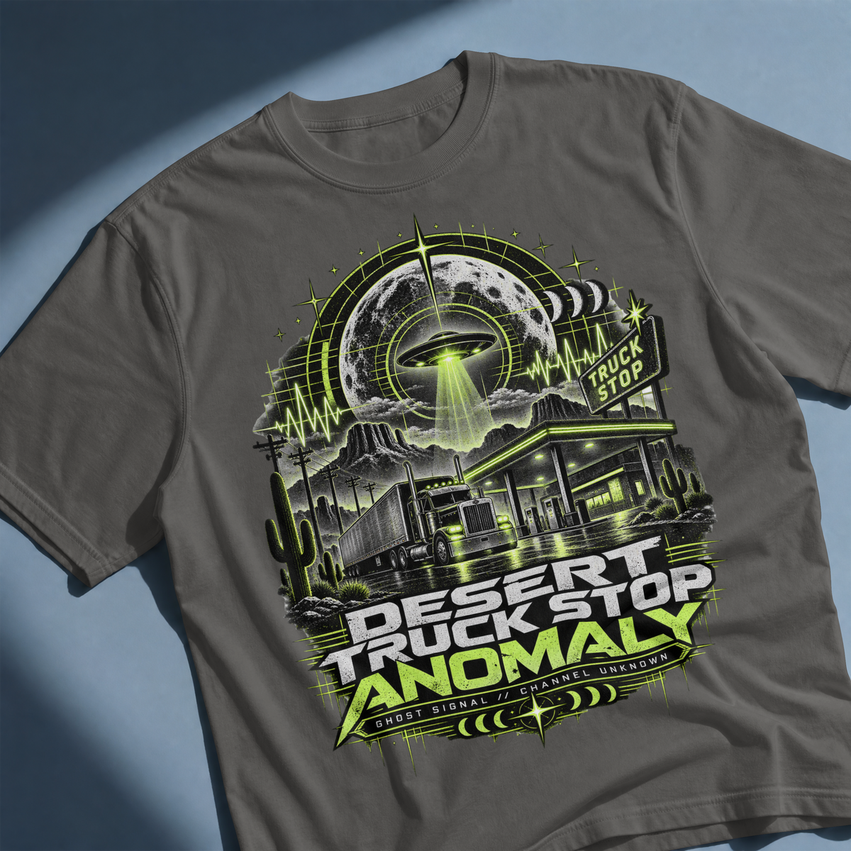 Angled close-up of the Desert Truck Stop Anomaly artwork on a Pepper T-shirt, showing the UFO, semi-truck and Ghost Signal // Channel Unknown text.