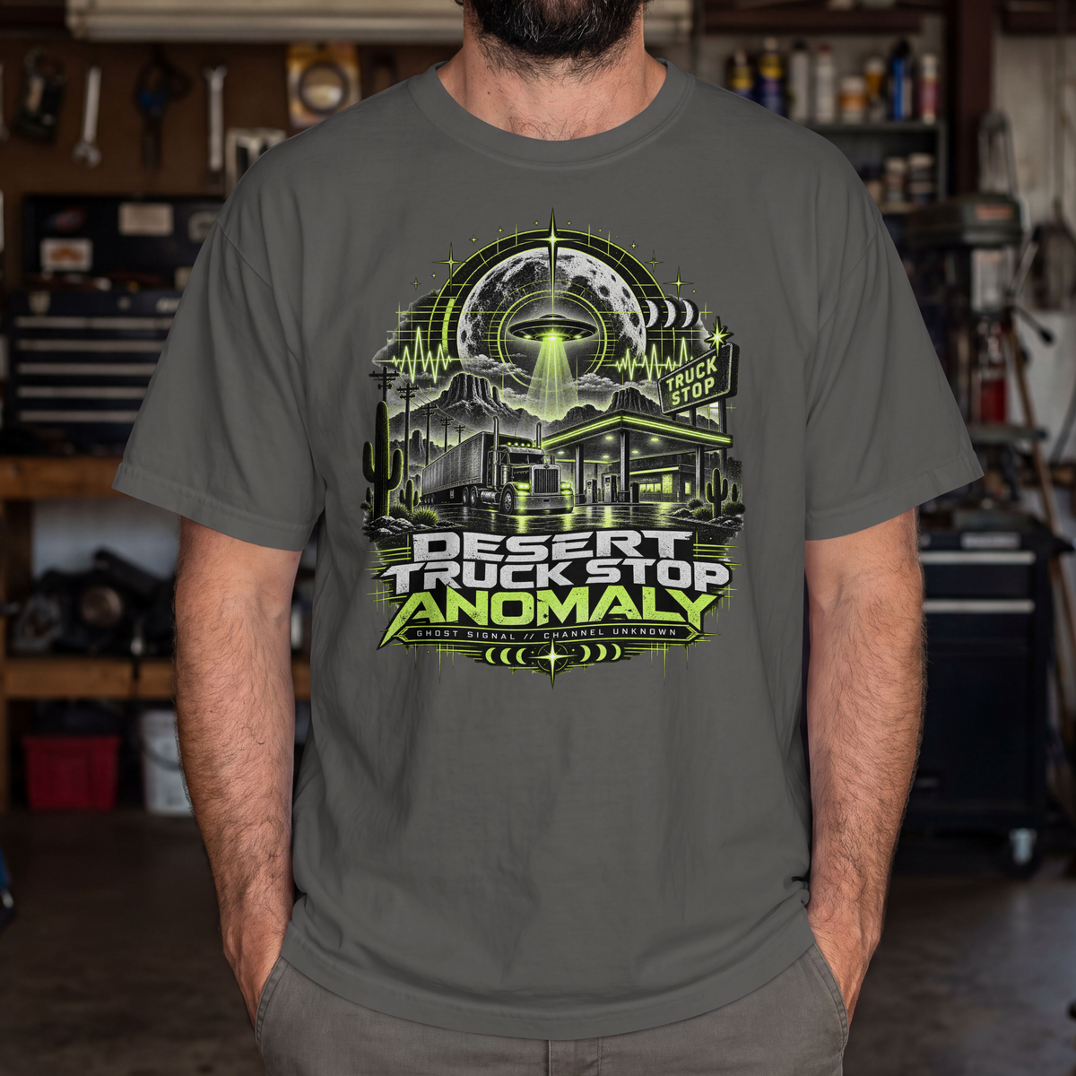 Pepper Desert Truck Stop Anomaly T-shirt worn by a male model, showing the green UFO, truck stop and semi-truck front graphic.