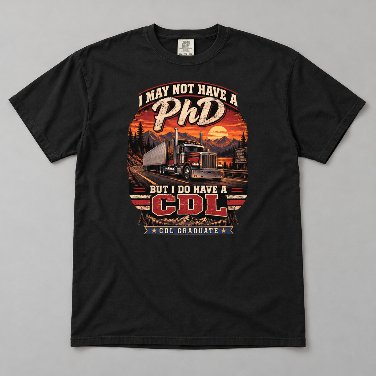 AI flat-lay mockup of a Black CDL Graduate T-shirt showing I May Not Have a PhD But I Do Have a CDL lettering, a red semi-truck, mountain-road sunset and two gold stars.