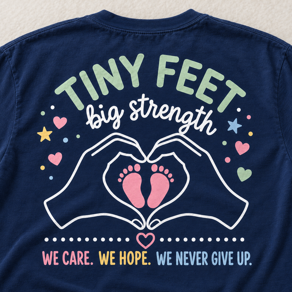 Close-up of the NICU shirt back artwork with baby footprints and We Care We Hope We Never Give Up lettering